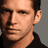Pixelated portrait of a person with short dark hair wearing a black shirt, next to bold white text on a black background.