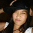 Pixelated image of a person wearing dark clothing and a black hat with light-colored trim, holding an object near their face.
