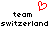 Red pixelated heart symbol above two 'team' texts and a repeated 'switzerland' text in black pixel font on white background.