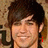 A static image of a person with dark hair and light skin, smiling against a textured background with partial text elements.