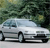 A silver sedan viewed from the side, positioned on a light gray surface with a blurred green foliage background.