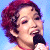 A pixelated split-screen image showing a person with short red hair holding a microphone on the left and green text reading "Original Icons .com" on a dark green background on the right.
