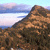 Pixelated landscape showing a brown rocky hillside under a light blue sky with horizontal cloud bands.