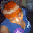 Pixelated image of a person with orange hair wearing blue clothing and holding a purple object against a dark background.