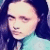 Pixelated close-up of a person with dark hair and light skin wearing a teal garment against a blue background.