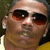A person wearing dark sunglasses and a yellow shirt appears in two side-by-side frames with slight variations in head position and ear visibility.