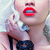 Pixelated close-up of a person with red lips, light skin, and dark hair, wearing a white top and dark pants, holding a white object near their face.