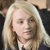 Pixelated close-up of a person with long light-colored hair, wearing a dark top with a light collar, against a blurred background.