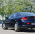 Pixelated image of a dark blue sedan with red taillights, positioned on a light-colored road against a blurred green background.