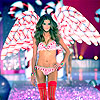 A model with long dark hair wears a pink and white polka-dot bikini top and bottom, red thigh-high boots, and large white-and-red patterned wings on a glittery runway.