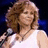 Pixelated image of a woman with curly brown hair wearing a white sleeveless top, holding a microphone against a dark blue background with overlaid blue text.