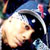 Pixelated static icon of a person's face with light skin tone, dark hair, and visible facial features against a dark background with blue and pink accents.