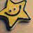 Yellow star-shaped icon with dark blue outline, smiling face featuring two eyes and a curved mouth on light brown background.