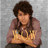 A person with curly brown hair wearing a maroon shirt holds arms crossed, displaying 'WOW' text on hands against a gray background.