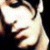 Pixelated close-up of a person's face with light skin tone, dark hair, and visible facial features including eyes, nose, mouth, and ear against a black background.