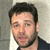 A pixelated close-up of a person with short dark hair, light skin, and a dark shirt against a light background.