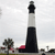 A static pixelated image shows a tall black-and-white striped lighthouse with a black top, set against a light gray sky, with a small tree and red-roofed building nearby.
