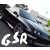 A blue sedan with visible headlights and grille is positioned on a road, with greenery and buildings in the background. White text 'GSR' appears below the car.