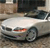 Static image of a silver sedan with a red taillight detail, positioned on a textured surface with blurred background elements.