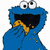 Blue Cookie Monster character with large white eyes and black pupils, holding a yellow cookie near its open mouth, with crumbs on its body and background.