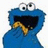 Blue cartoon character with large eyes and open mouth holding a cookie, set against white background with blue text reading WANT COOKIE.