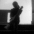 Silhouette of a person holding a guitar-like instrument, standing near a window with a dark interior background.