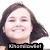 A pixelated image of a smiling person with long dark hair, wearing a dark top, with a black bar containing partial text at the bottom.