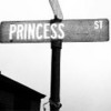 Black-and-white street sign with 'PRINCESS' and '51' text on a horizontal pole, mounted on a vertical post with partial building roof visible below.