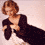 A woman with short curly blonde hair wears a dark long-sleeve dress against a light background, shown in two cropped views with different poses.