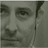 Static grayscale icon of a person's face with visible pixelation and dithering, showing partial facial features including eyes, nose, mouth, and hair against a neutral background.