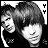 Black-and-white pixelated image of two people with dark hair, one smiling broadly and the other with a neutral expression, set against a checkered background with two black Y-shaped symbols.