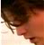 Pixelated close-up of a person's face with dark hair, wearing a red garment against a light background.