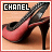 A red high-heeled shoe with black straps and a stiletto heel, displayed under the text 'CHANEL' on a light brown background.