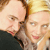 Two people in close proximity with light skin tones, one wearing dark clothing and the other in light tones, against a blurred background with warm colors.
