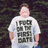 Pixelated image of a person wearing a white T-shirt with large dark blocky text on the chest, standing against a dark background.