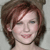 Pixelated close-up of a person with short brown hair, closed eyes, and a slight smile against a light gray background.