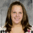 A pixelated image of a smiling woman with long brown hair, wearing a white top with dark patterns and pink accents, set against a gray background.