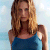 A pixelated static image of a person with long brown hair wearing a blue sleeveless top against a light blue background.
