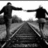 Black-and-white image of four figures holding hands on railroad tracks, with one figure missing in the bottom-left view.
