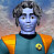 Pixelated figure with light blue skin, dark curly hair, and a teal uniform with orange shoulder accents and a yellow circular emblem.