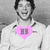 Pixelated grayscale image of a person with dark hair wearing a white shirt and pink heart-shaped graphic on chest.