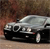 A silver sedan with black lower body panels is positioned at a three-quarter angle against a blurred brown background.