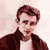 Static pixelated image of a person with brown hair wearing a dark jacket over a light shirt against a pale background.