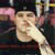 A pixelated image shows a person with dark hair and light skin, wearing a dark shirt against a blurred background.