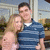 A couple in a blue striped polo shirt and pink top pose together outdoors with blurred background elements.