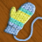 Pixelated image of a mitten with yellow, teal, and light blue sections on brown background.