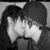 Two people in close physical proximity with dark hair, one wearing a cap, sharing an intimate moment