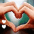 A hand forms a heart shape around a green and white object with small white hearts on the left side.