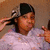 A person in a light purple shirt and dark headwrap adjusts their hair with both hands, while pink text overlays appear sequentially.