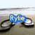 Pixelated image shows a blue speech bubble with white text 'Rylie' over dark circular objects on a sandy background under light sky.